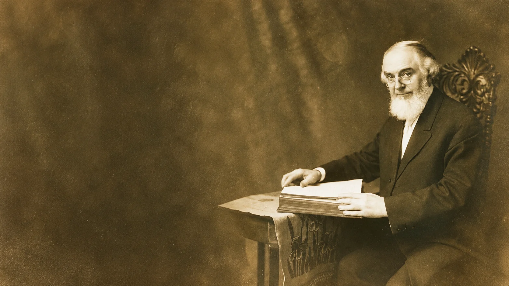 Charles Taze Russell sentado ante un libro, en un retrato fotográfico de 1911 adaptado a formato apaisado.